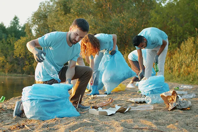Volunteering abroad group cleaning a beach, collecting trash in blue bags, showing active travel style and environmental care.
