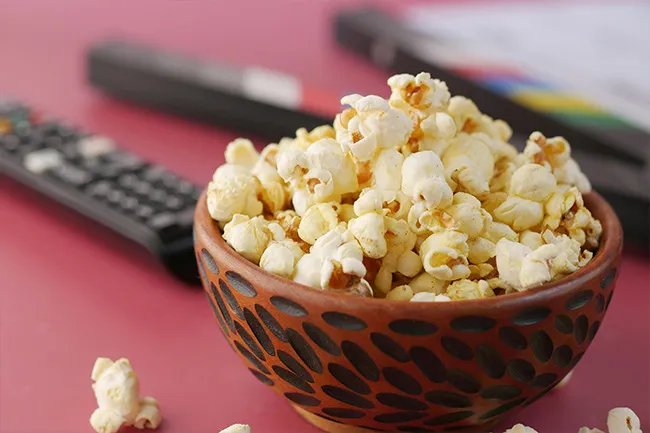 Bowl of popcorn on a table with a TV remote in the background, a popular nervous snack choice.