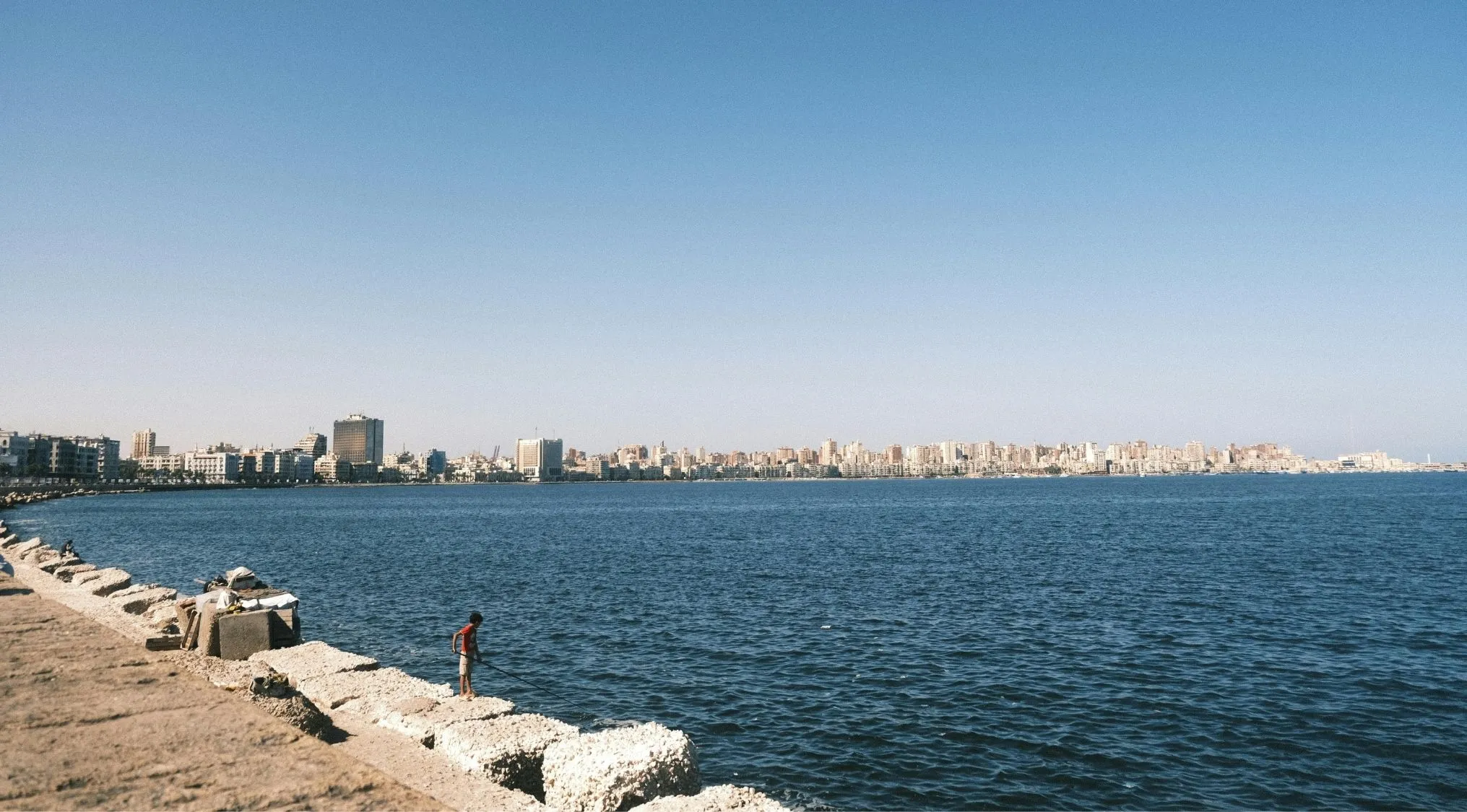 Coastal view of Alexandria city in Egypt with a person standing on rocks by the water, highlighting commonly confused countries.