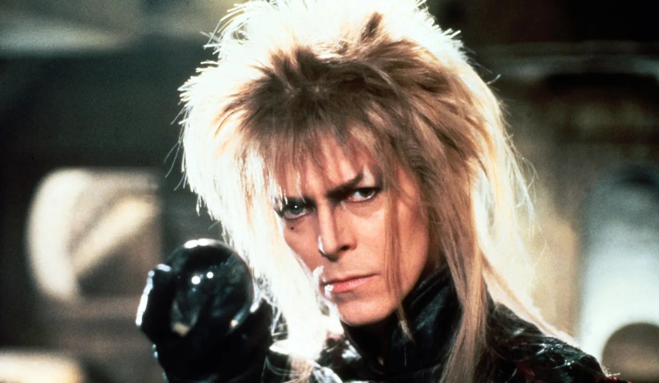 80s and 90s music icon with spiked blond hair and intense gaze holding a dark crystal orb in a dramatic scene.
