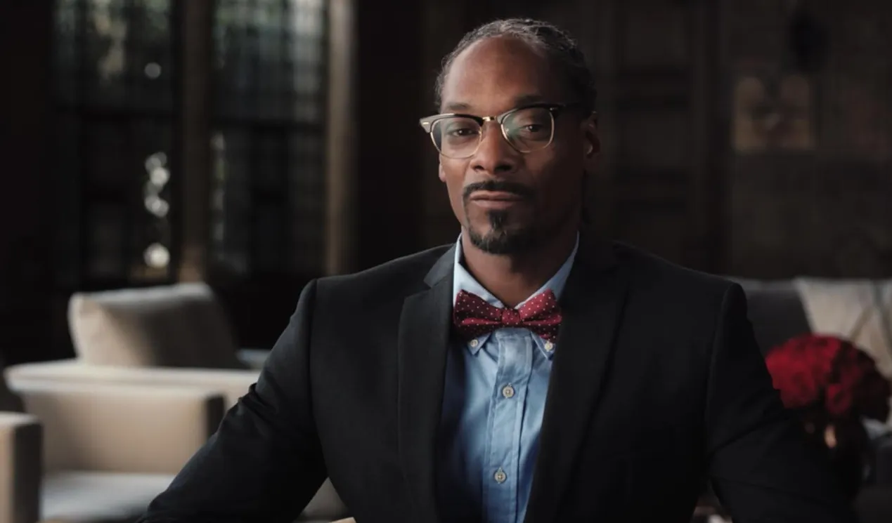 Male music icon from the 80s and 90s wearing a suit, glasses, and a red bow tie in an elegant indoor setting.