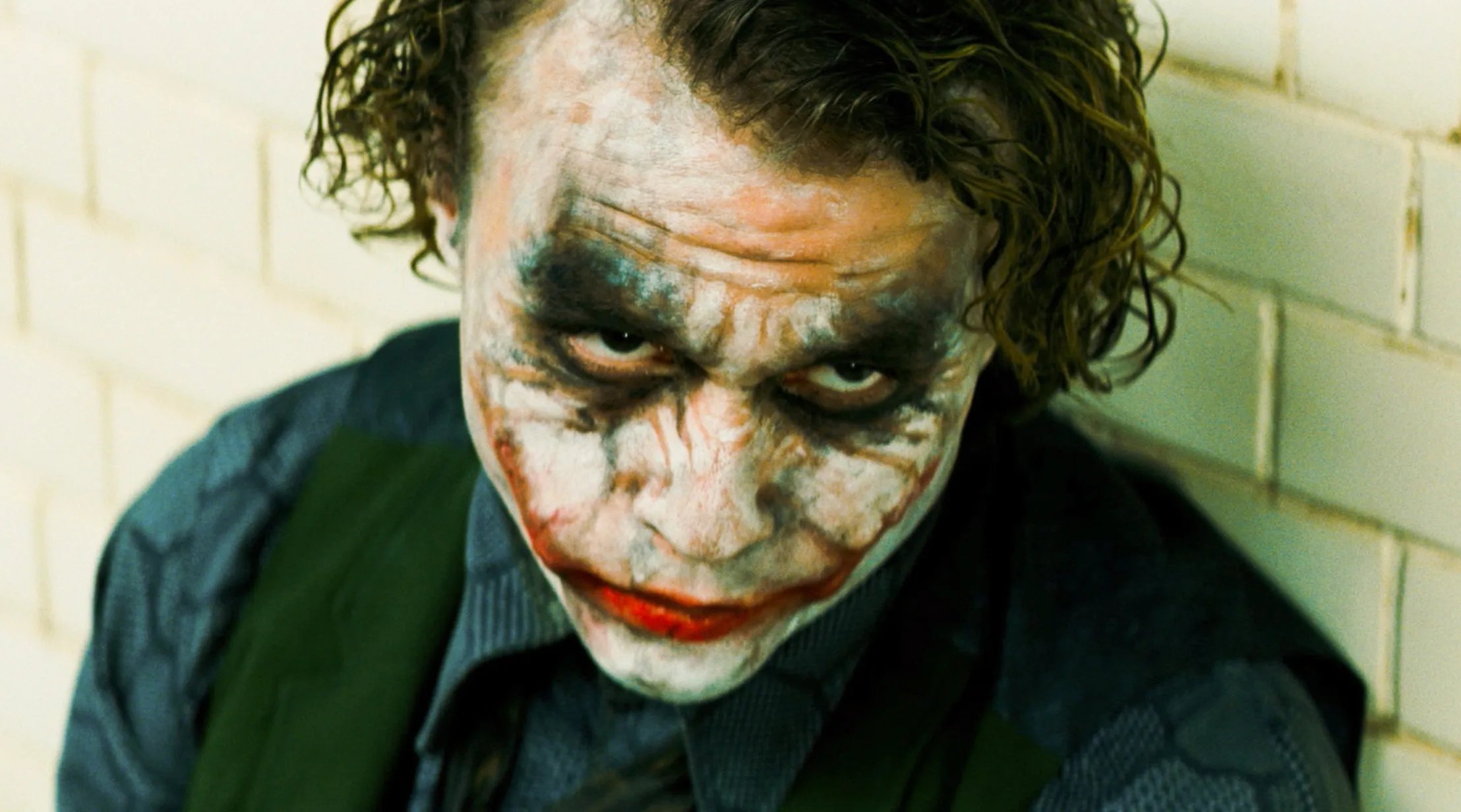 Heath Ledger as the Joker in The Dark Knight, with white face paint, smudged makeup, and intense expression.