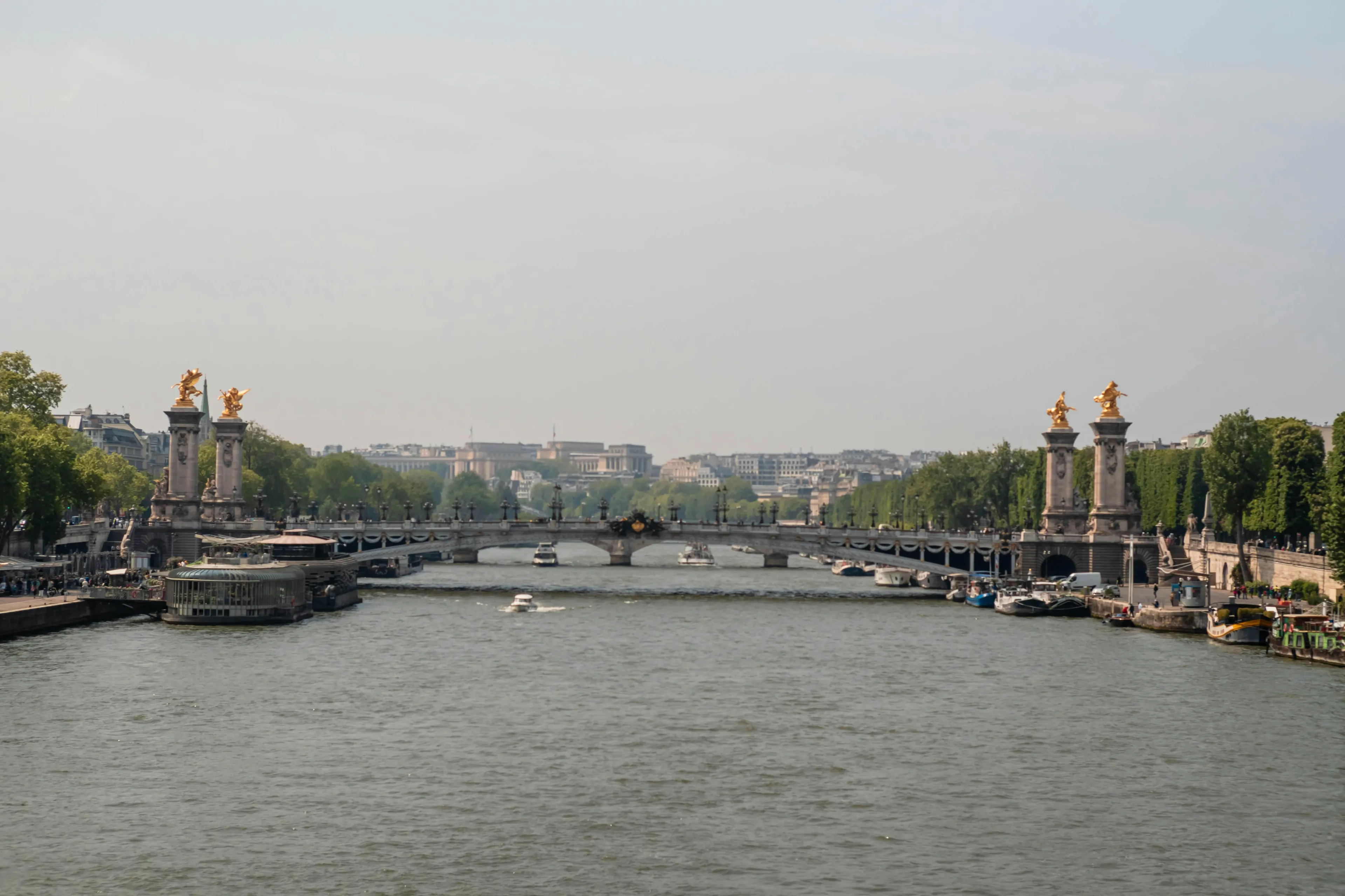 The Seine river flowing through Paris with historic bridges, boats, and green trees along the riverbanks on a clear day.
