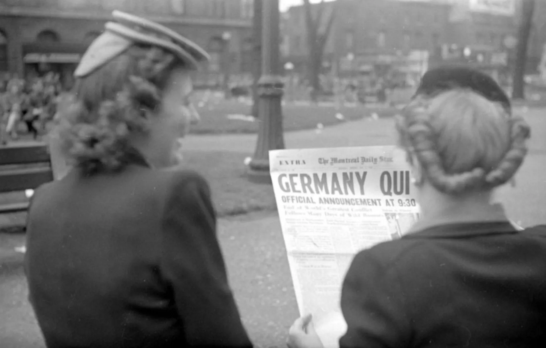 Two women in vintage clothing reading a newspaper with Germany quit headline, relating to World War II end year quiz.