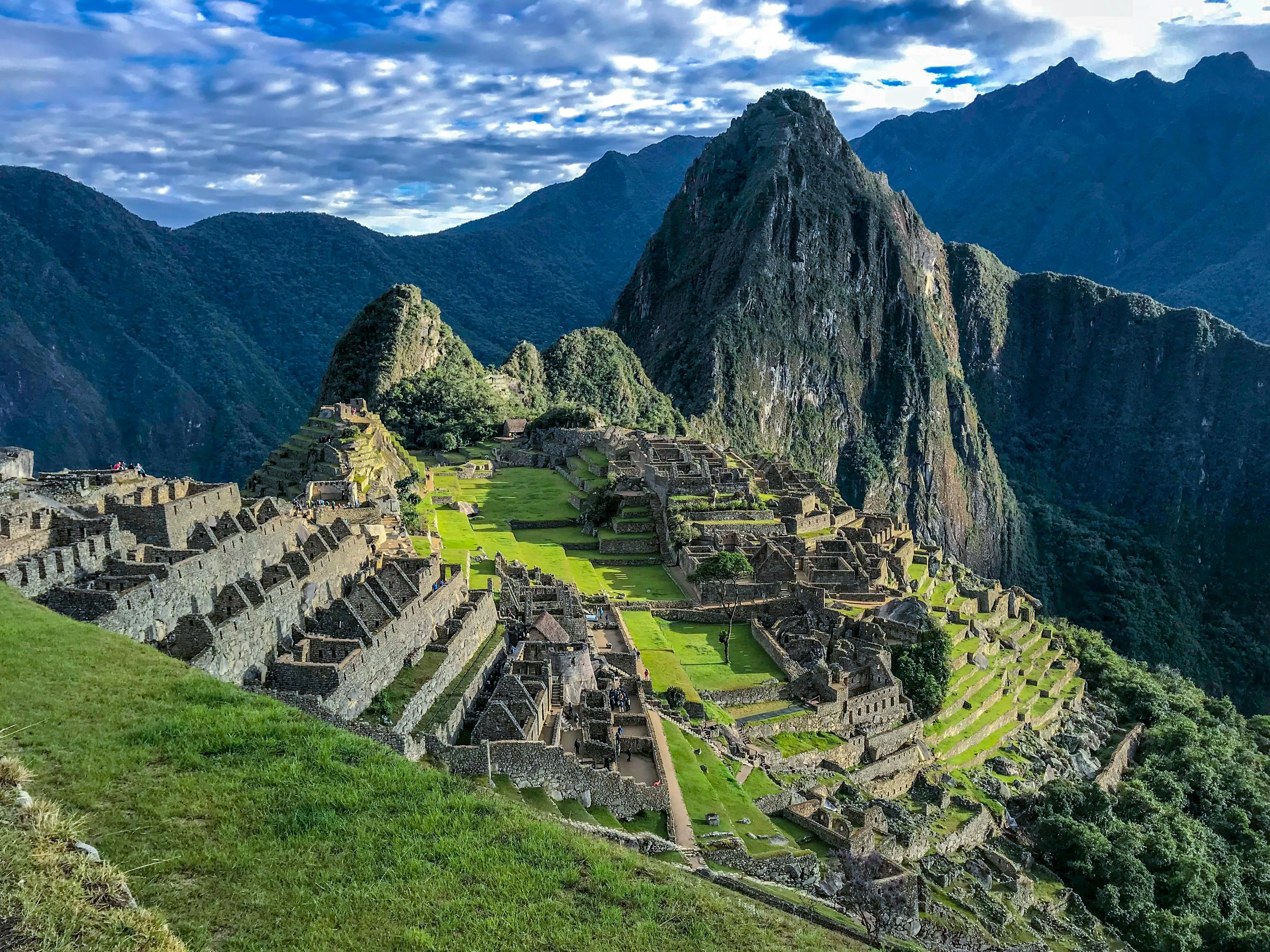 Machu Picchu ancient citadel in Peru with green terraces and surrounding Andes mountains under blue sky.