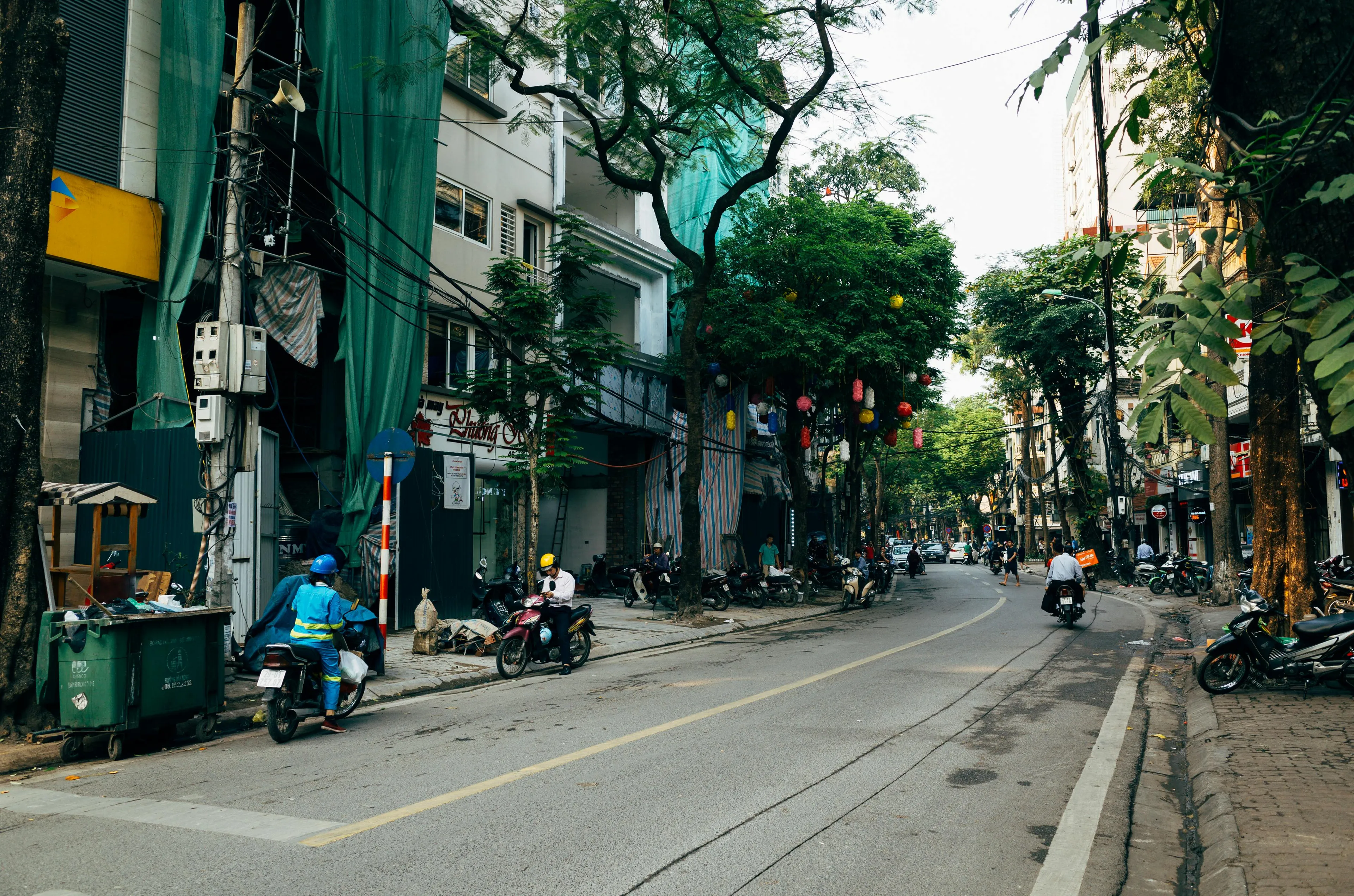 Busy street scene in Hanoi with scooters, urban buildings, and trees showcasing the geography of this Vietnamese city.