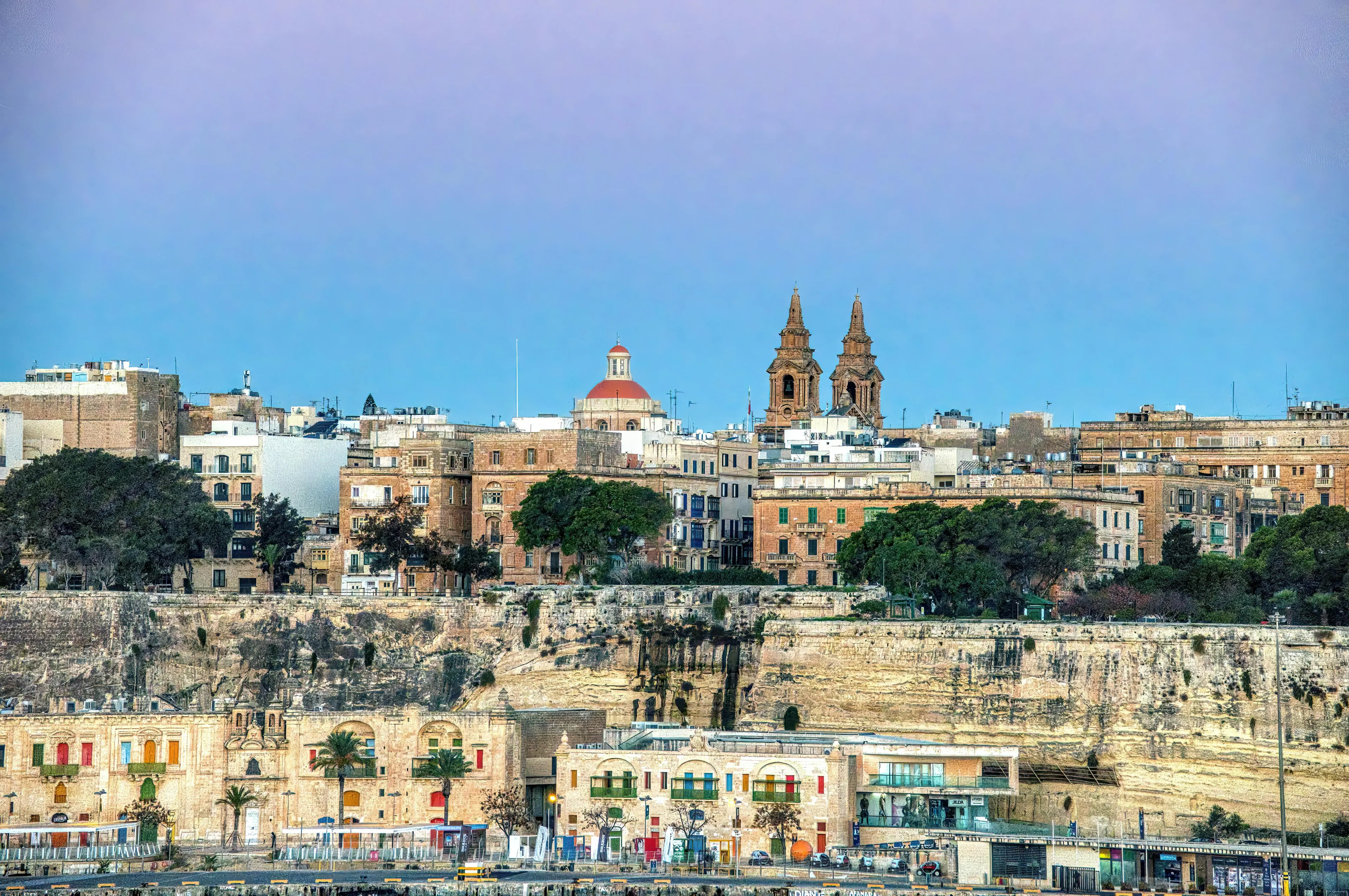 View of Valletta, the capital city of Malta, showcasing historic buildings and coastal cliffs at sunset.
