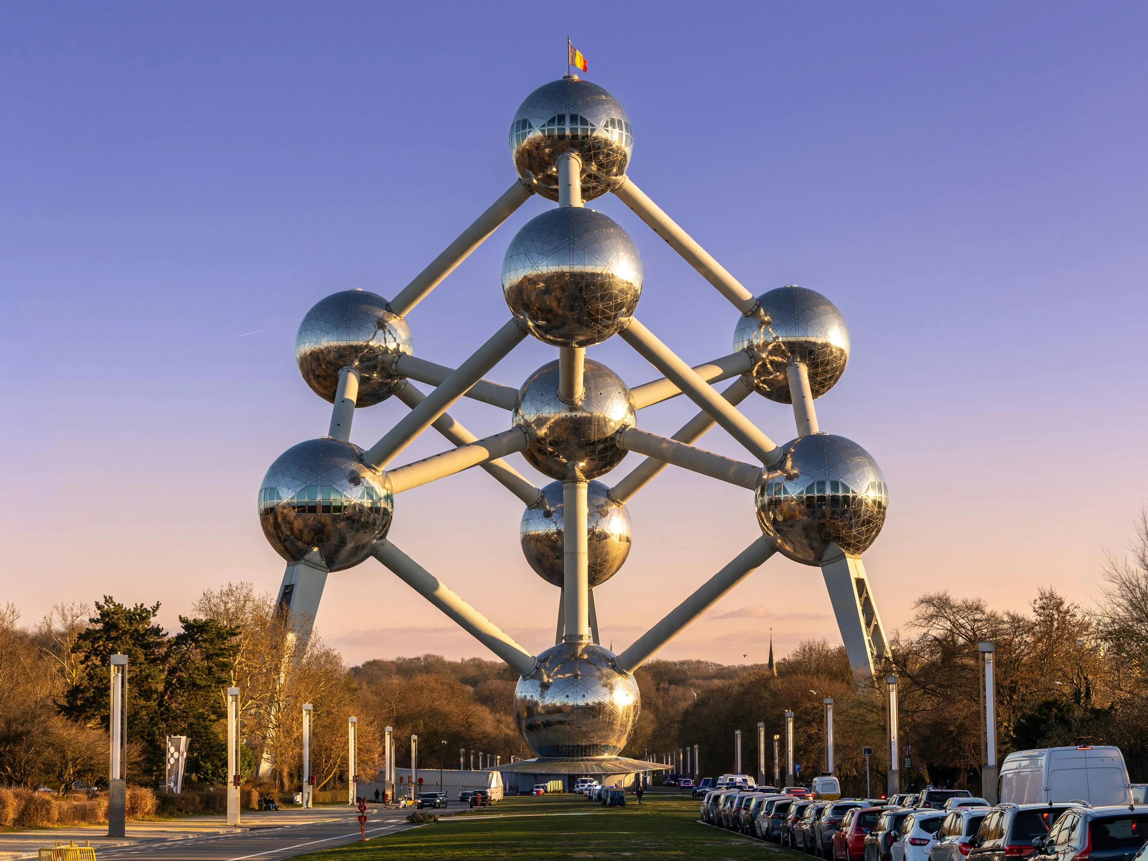 Reflective large steel spheres connected by tubes forming a scientific structure, symbolizing subatomic particle concepts with positive charge.