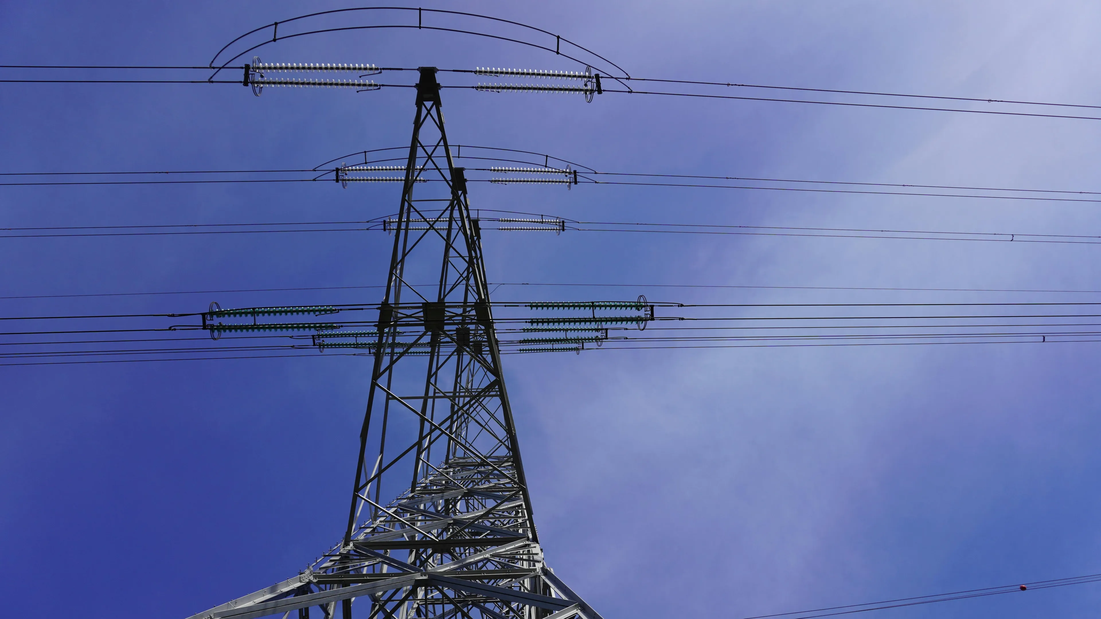 High voltage power lines on a metal electricity conductor tower under a clear blue sky.