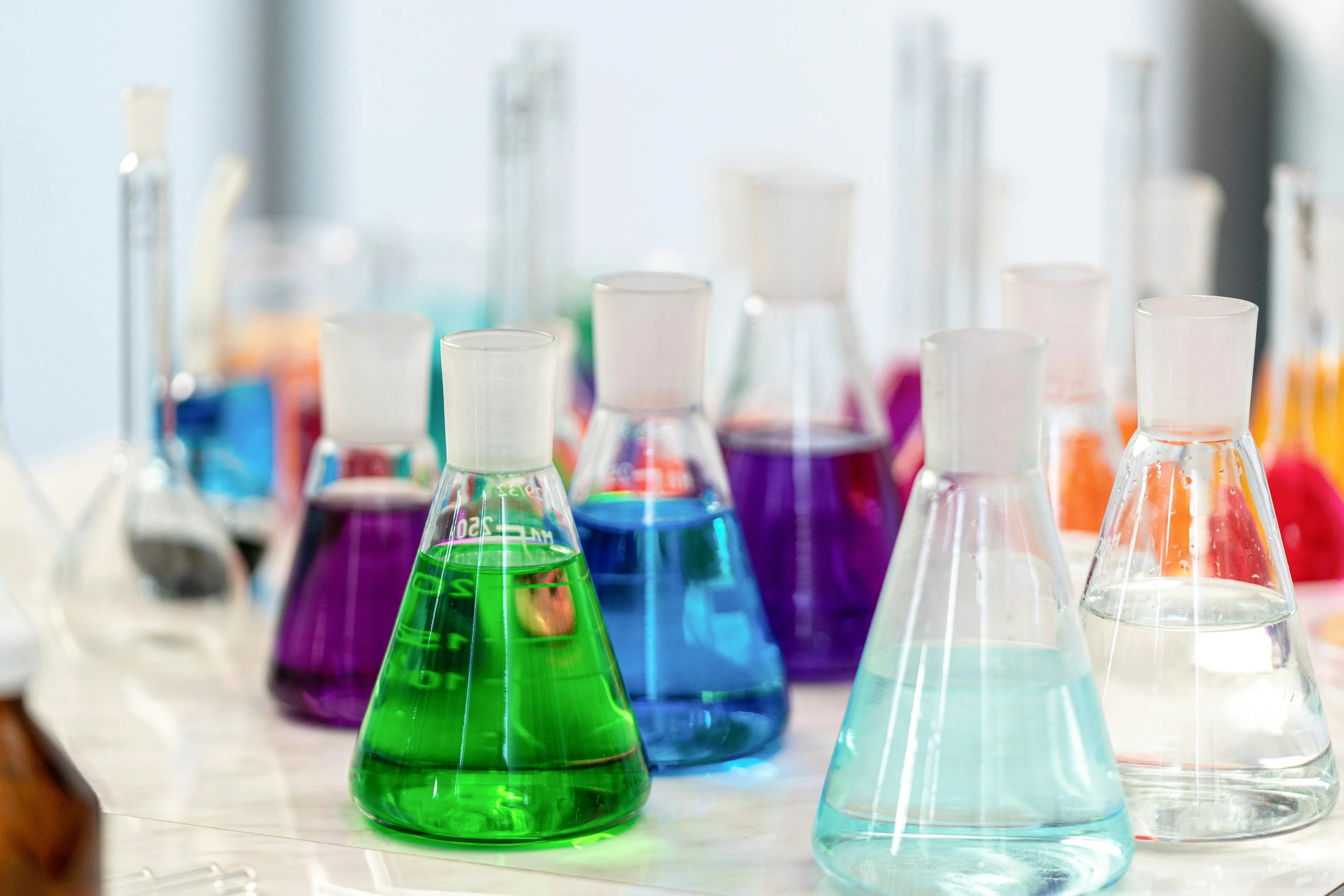 Laboratory Erlenmeyer flasks filled with colorful aqueous solutions illustrating pH value concepts in science.