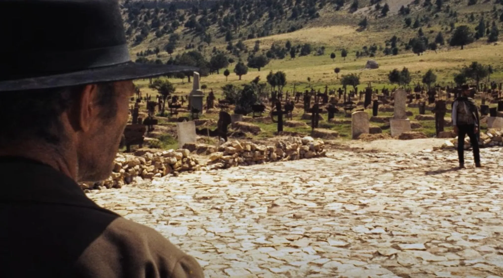 Two men in a dusty cemetery scene, classic 60s movie scene with a standoff setting and vintage Western attire.