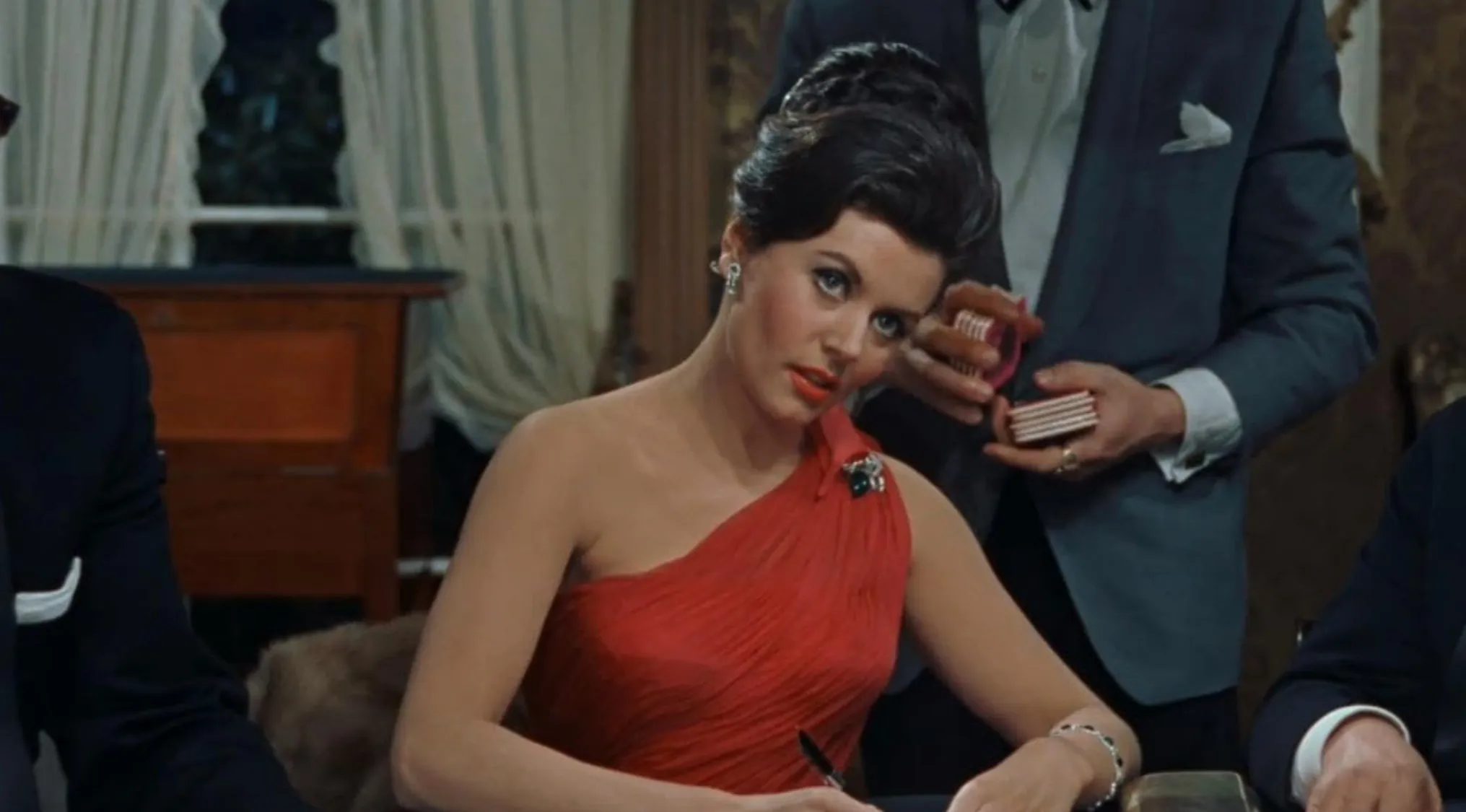 Woman in a red dress at a table with men in suits, a classic 60s movie scene from a 1960s film setting.