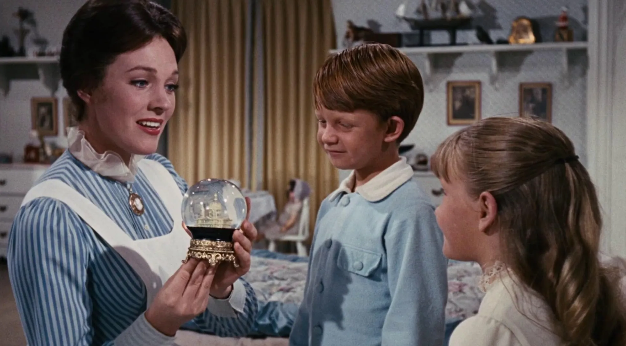 Woman showing a snow globe to two children in a 60s movie scene inside a vintage bedroom setting.