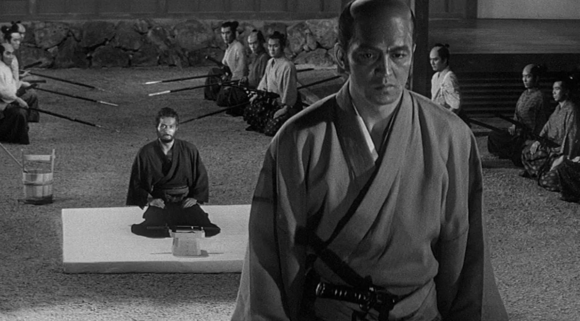 Black and white scene from a 60s movie with samurai warriors in traditional clothing during a tense gathering.