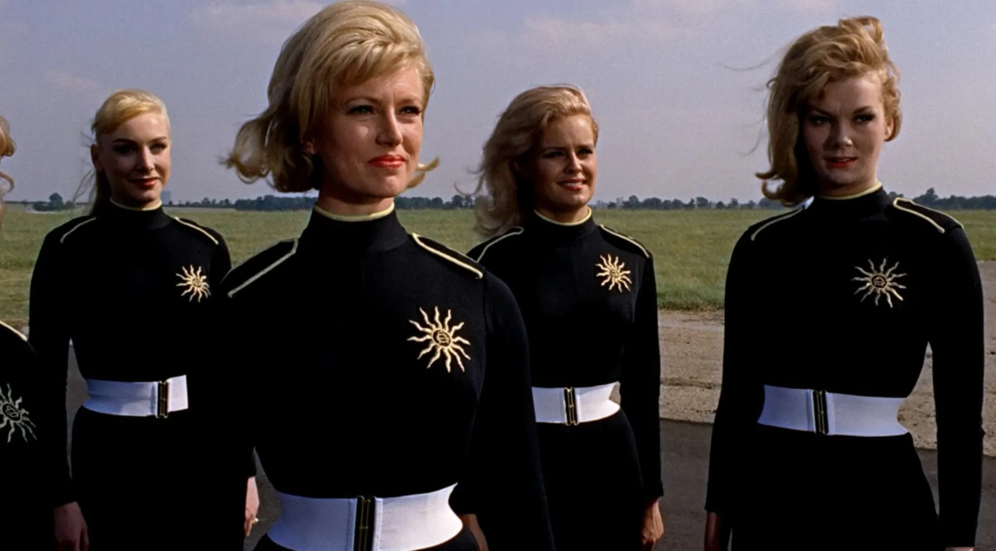 Women dressed in black uniforms with white belts in an outdoor scene from 60s movie scenes to uncover.