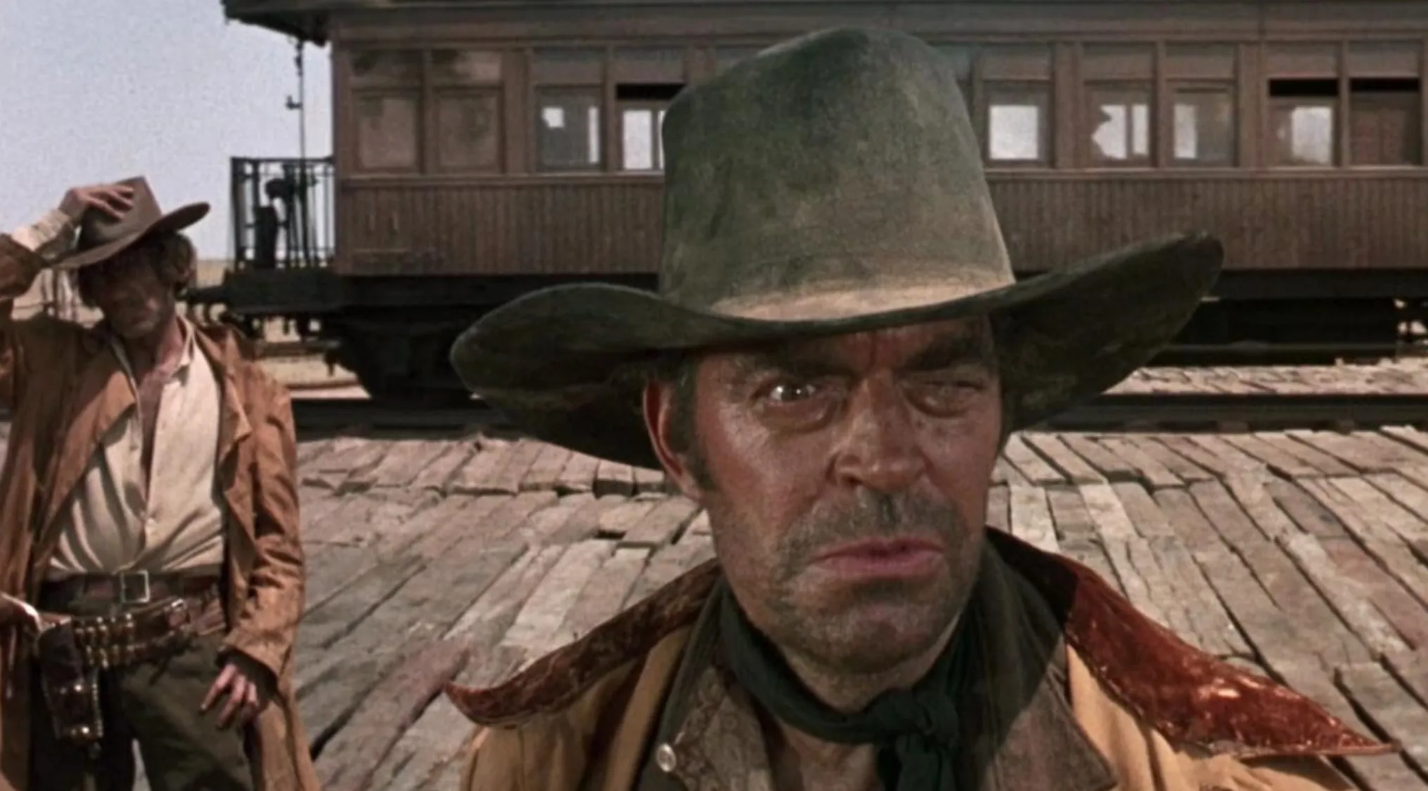 Close-up of two cowboys in a classic 60s movie scene with old train in the background, iconic western setting.
