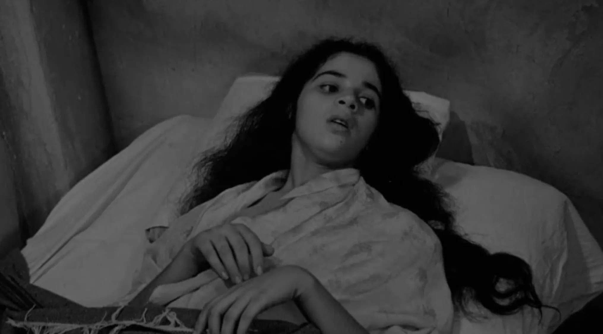 Woman with long dark hair lying on a bed in a black and white 60s movie scene for you to uncover.