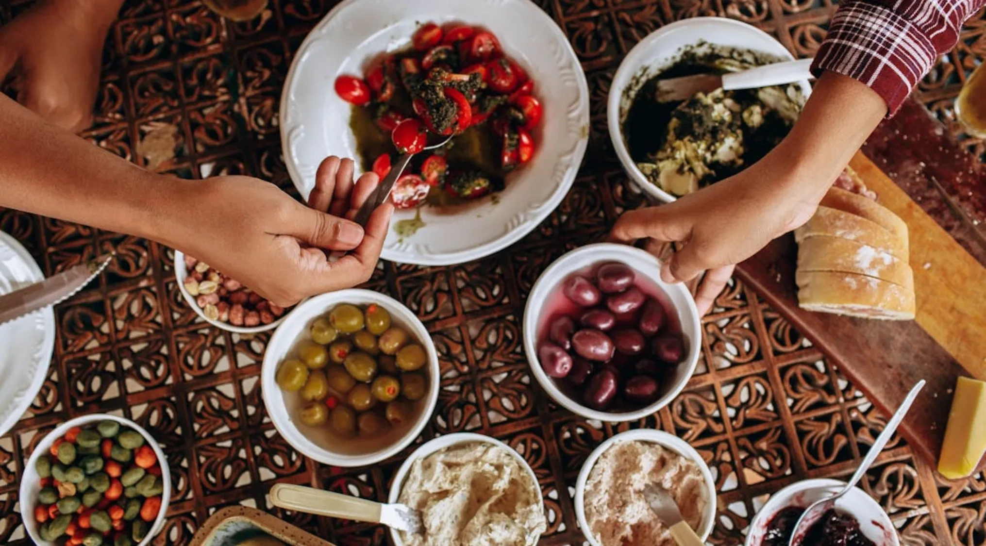 Hands serving olives and Mediterranean dips on a table, representing food of the gods in Greek mythology.