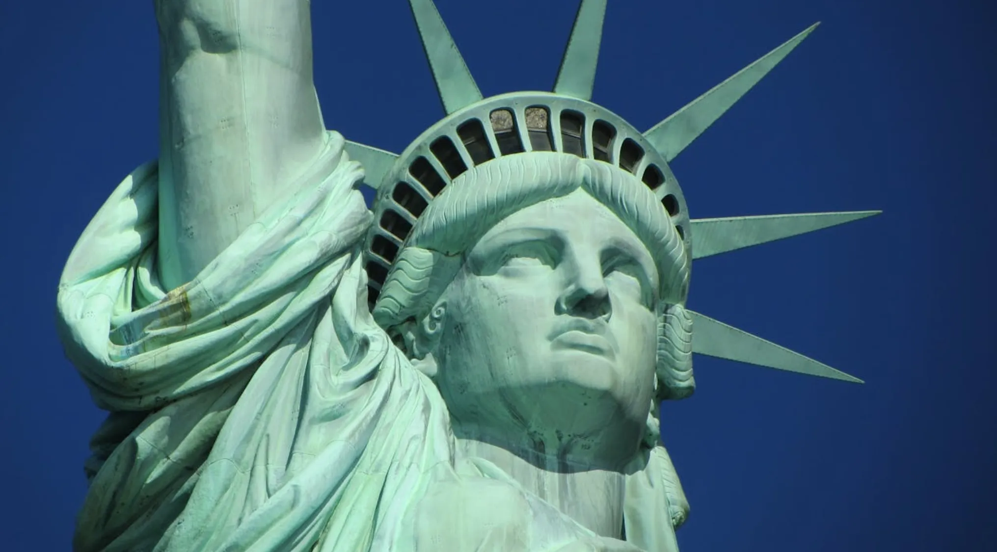 Close-up of the Statue of Liberty's face and crown against a clear blue sky.