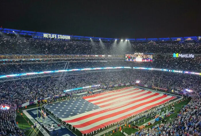 Large crowd at MetLife Stadium holding a giant American flag, showcasing intelligence in creative public displays.