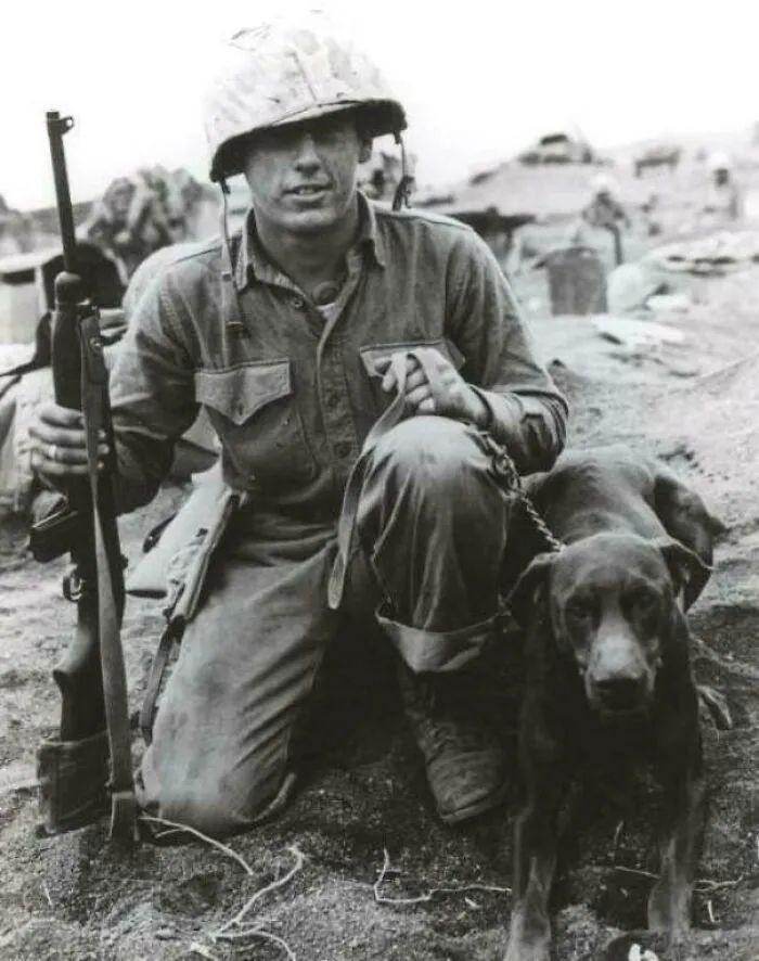 A soldier kneeling with his dog and a rifle, an emotional historical photo of companionship during conflict.