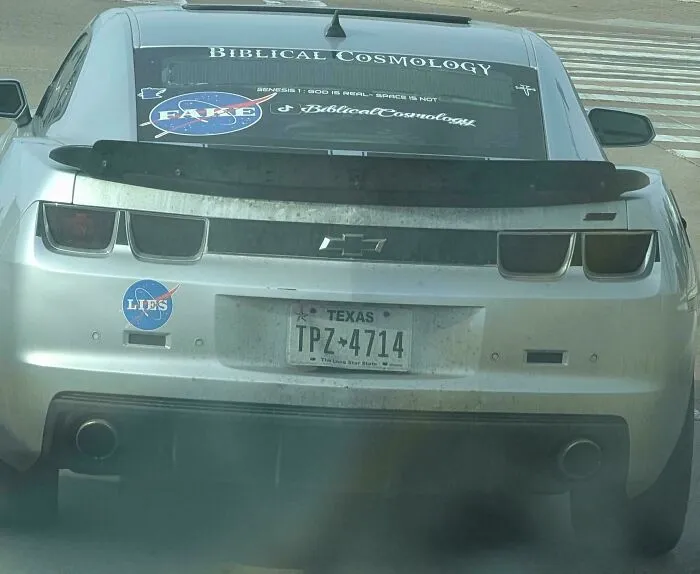 A car with unfiltered bumper stickers on the back window and bumper, including NASA IS FAKE and LIES.