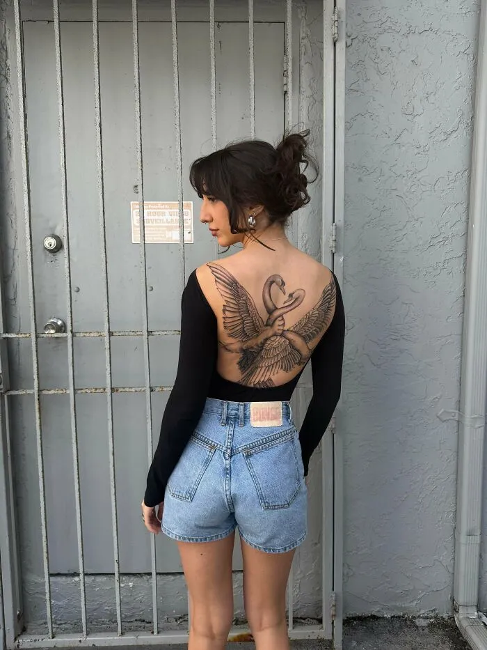 A woman with an elaborate back tattoo of two swans with interlocking wings, showcasing beautiful tattoos.