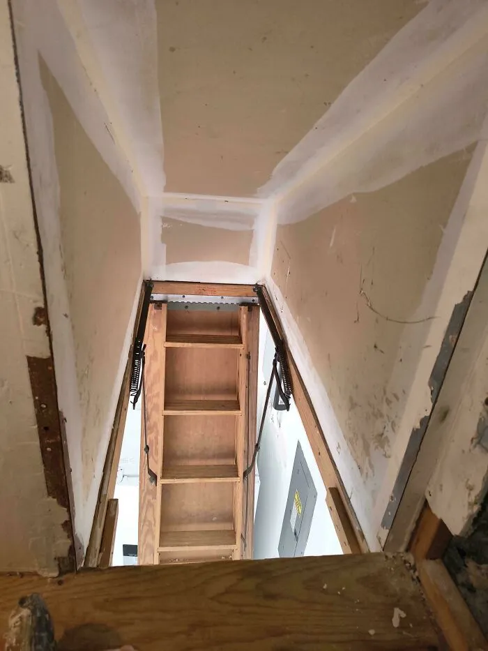 A questionable DIY project showing an unsafe attic ladder setup through a drywall opening.