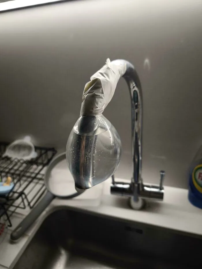 Kitchen faucet taped with a water-filled plastic bag in a funny DIY repair.