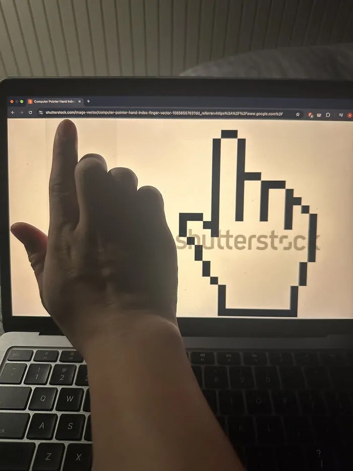 A hand pointing at a computer screen showing a pixelated hand cursor, from the Not Interesting Community.
