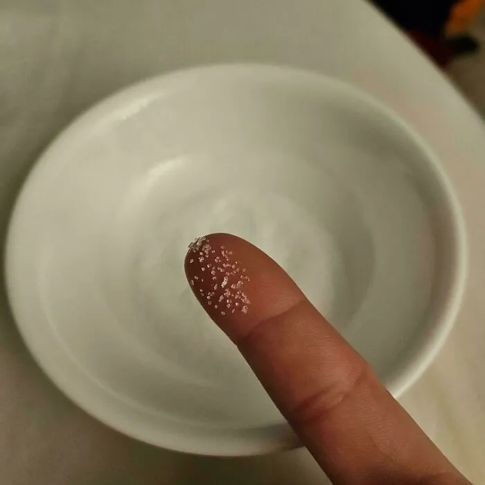 A finger with a few grains of sugar on it, over a white bowl, a picture from the Not Interesting community.