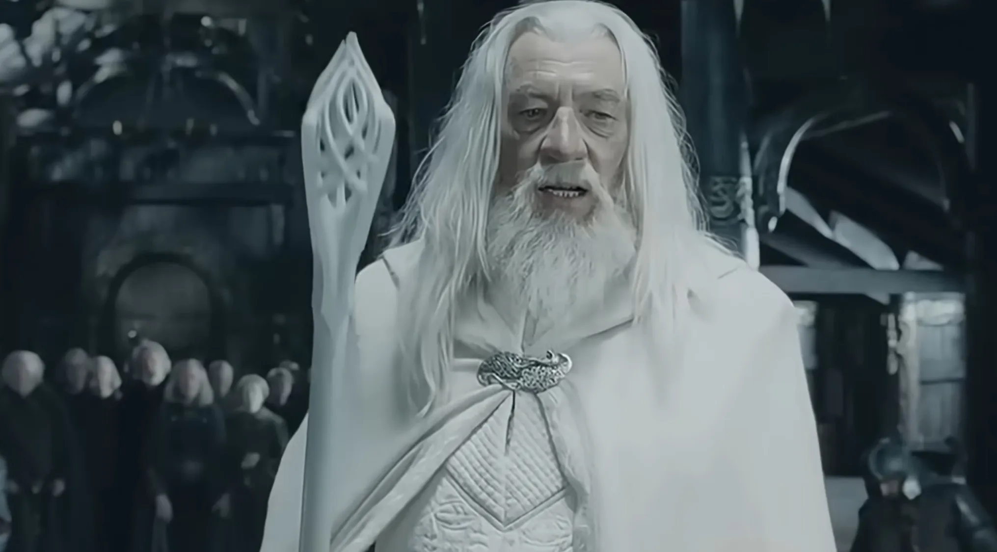 Gandalf the White holding his staff in a white robe with people blurred in the background guessing sold item prices.