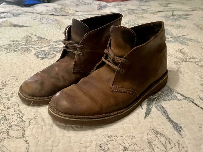 Pair of worn brown leather desert boots resting on a patterned bedspread, representing old products.