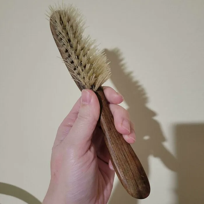 Hand holding a durable vintage wooden hairbrush with natural bristles, showing old products still in use.