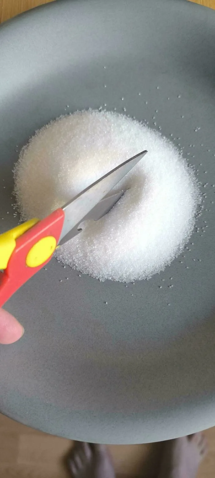 A pair of scissors cutting into a pile of white sugar on a gray plate, illustrating a not interesting moment.
