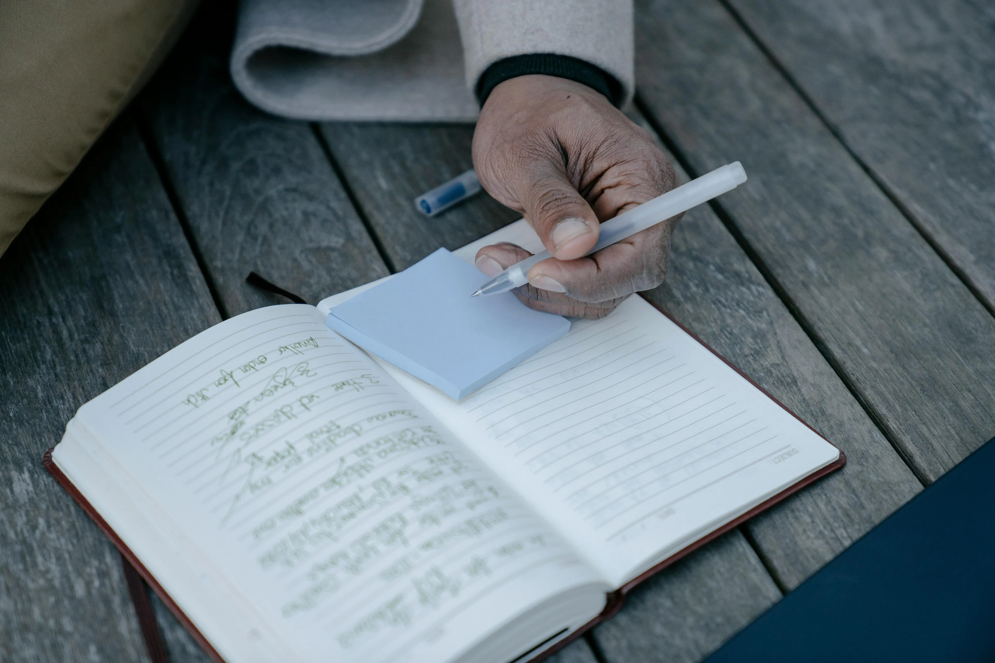 Person writing in a journal on a wooden table, choosing a rainy-day activity with pen and notebook.