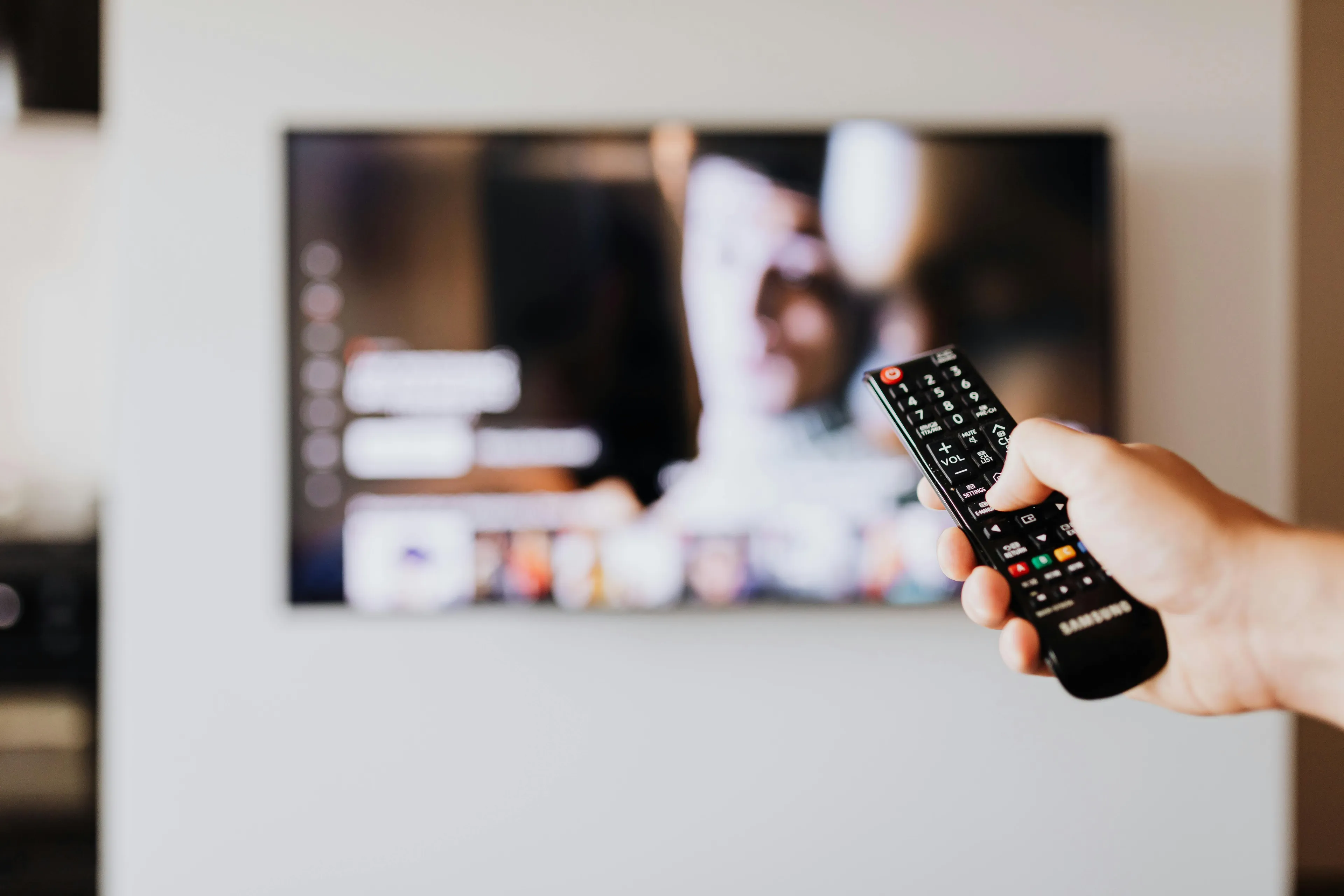 Person holding a remote control, rewatching a comfort movie on TV as a rainy-day activity at home.