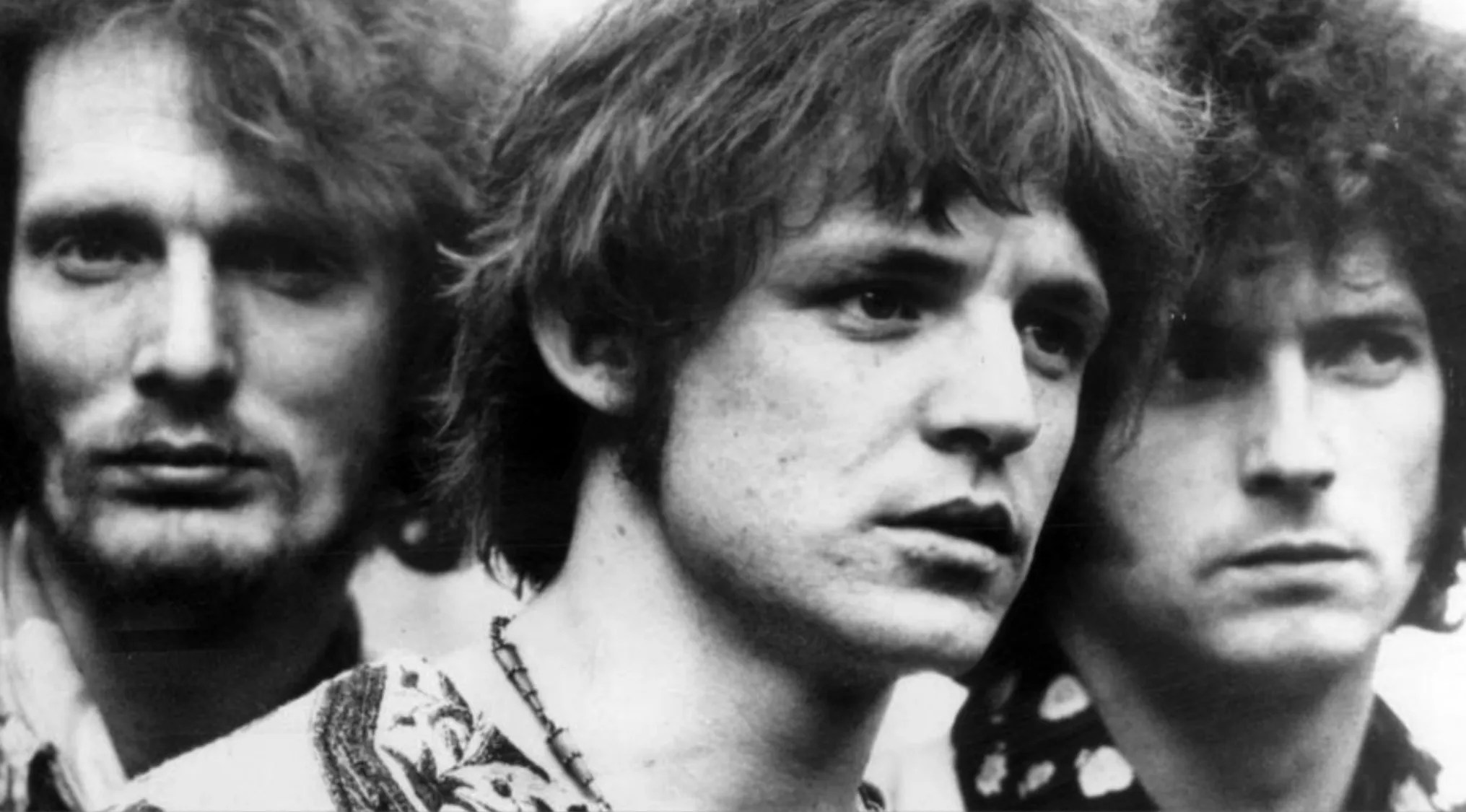 Black and white portrait of the band Cream members with intense expressions in a close-up photo.