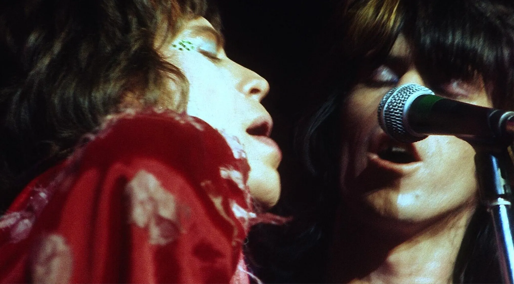 Mick Jagger and Keith Richards singing closely into a microphone during a live performance on stage.