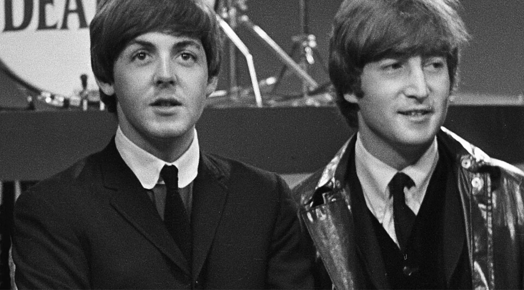 Paul McCartney and John Lennon of the Beatles posing together during a musical performance in black and white.