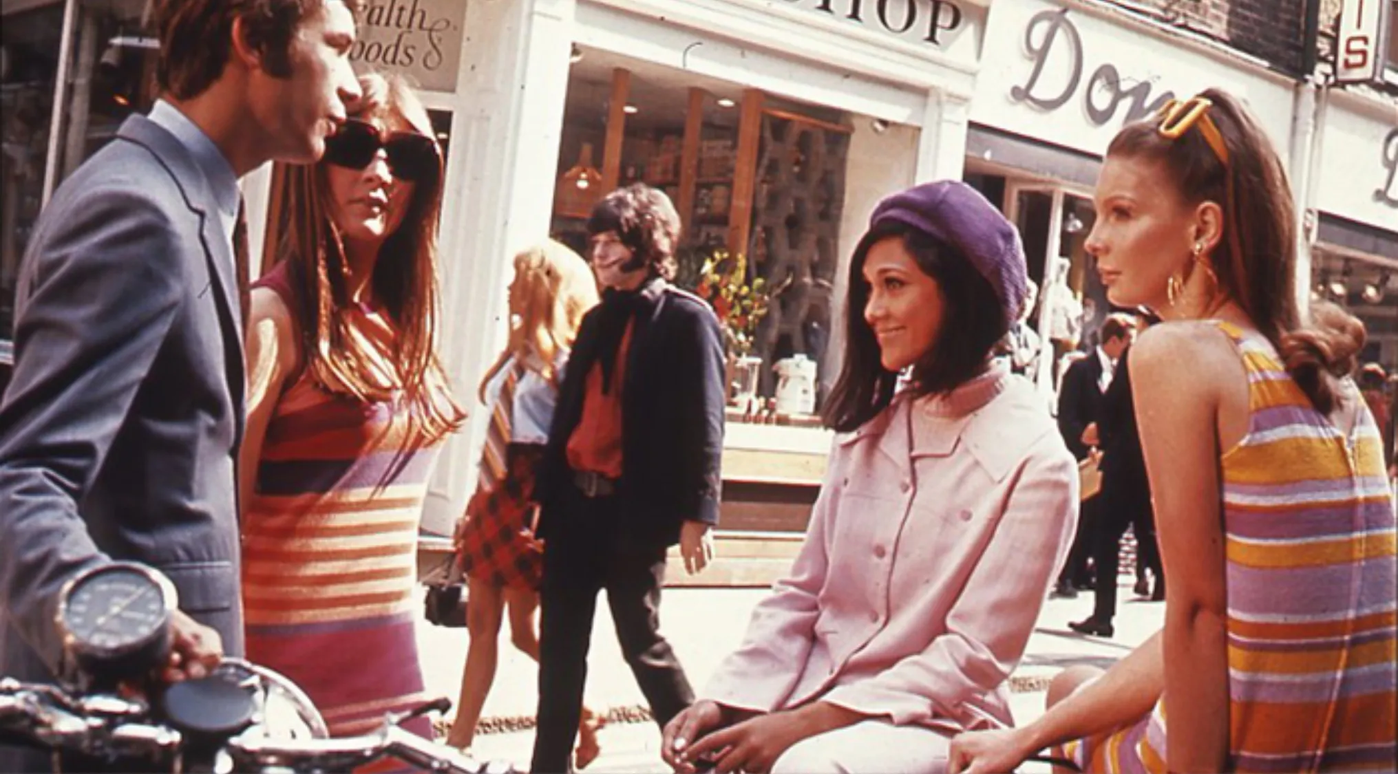Group of people wearing colorful striped and mod fashion styles iconic to London’s Swinging Sixties street scene.