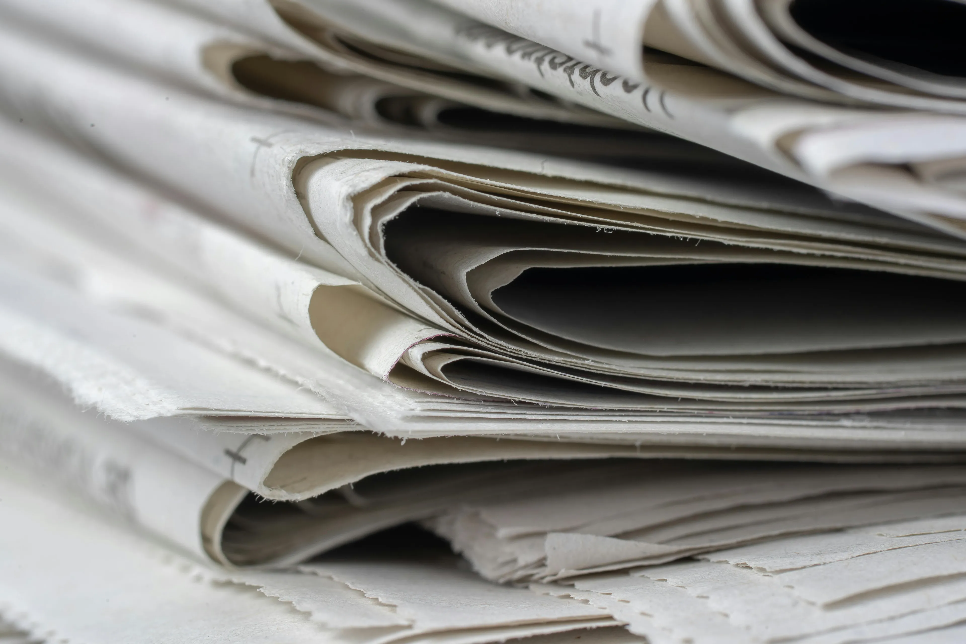 Close-up of a freshly printed newspaper stack highlighting the texture and folds of newsprint paper.