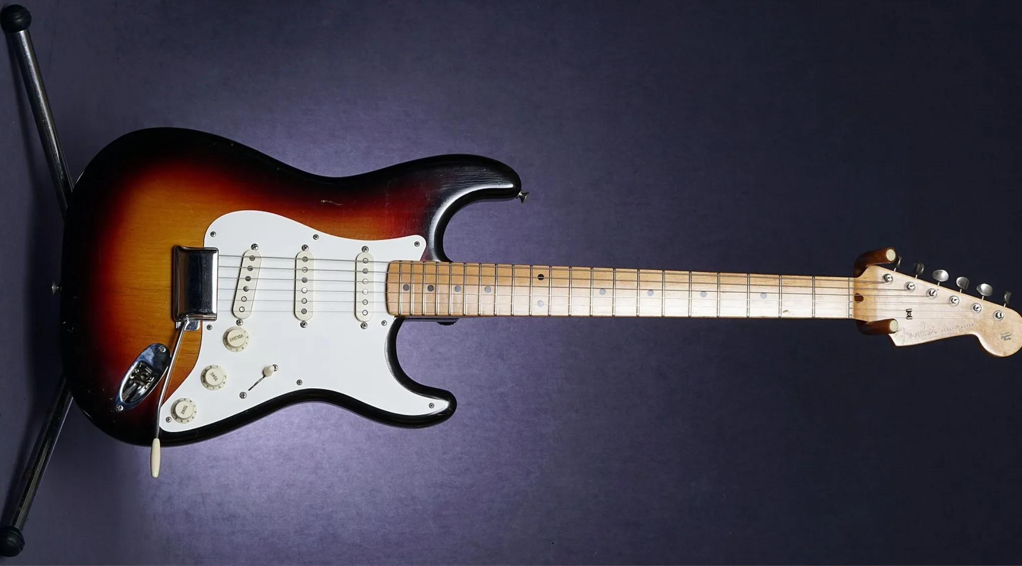 Sunburst Fender Stratocaster electric guitar with white pickguard and maple neck against a dark background