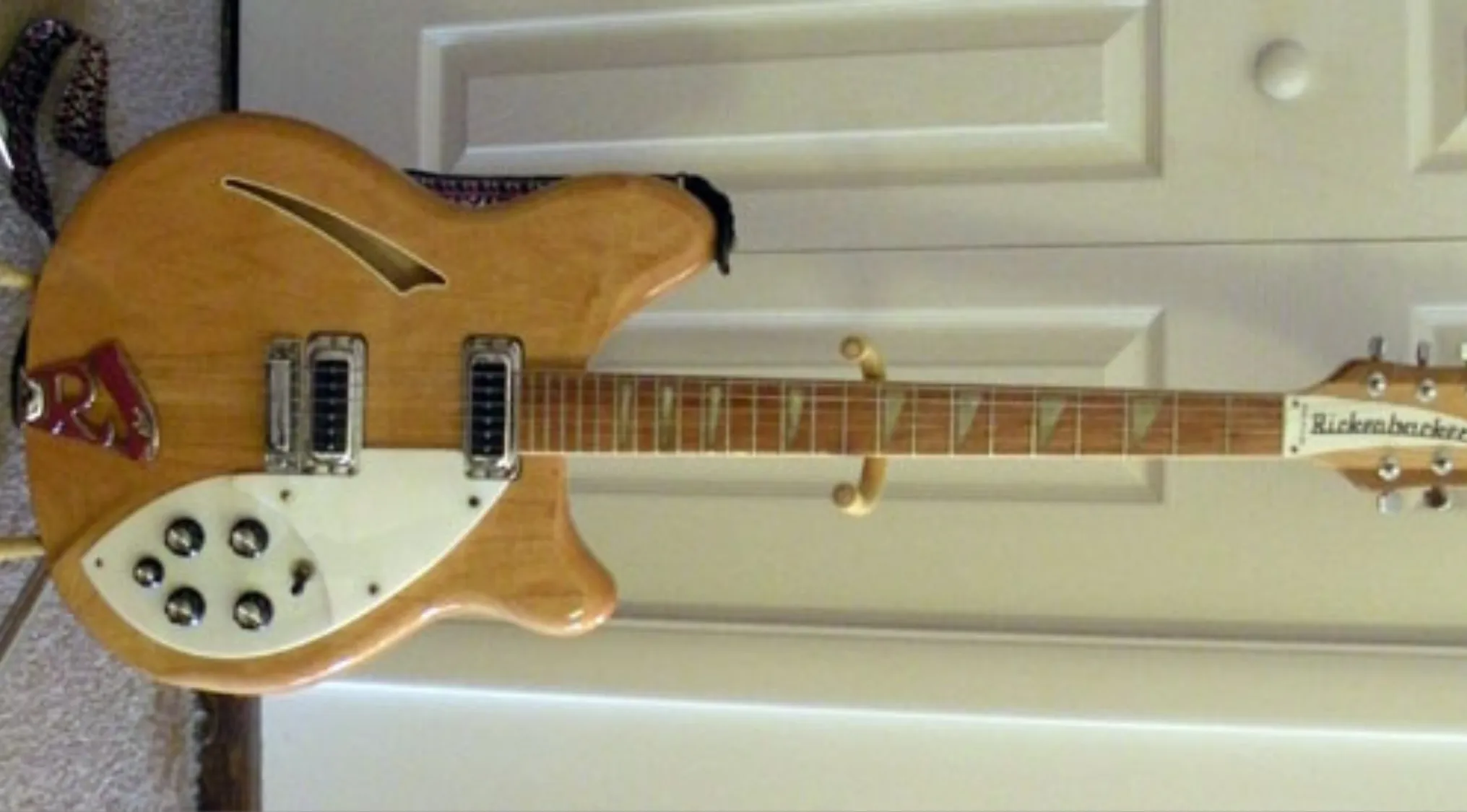 Natural wood finish Rickenbacker 360 electric guitar leaning against white paneled doors indoors.