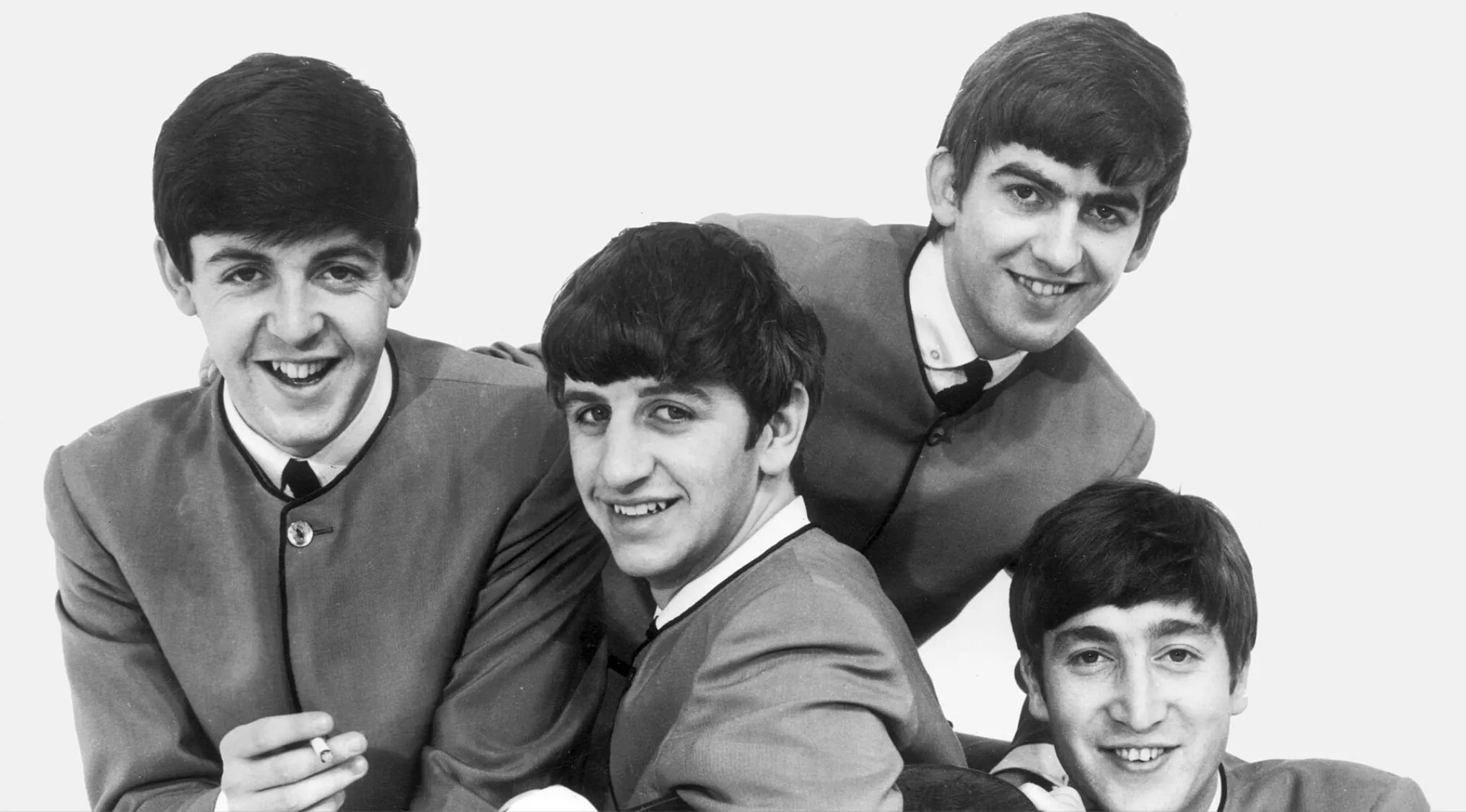 The Mop Top Beatles members smiling in classic suits with mop top hairstyles in a black and white photo.