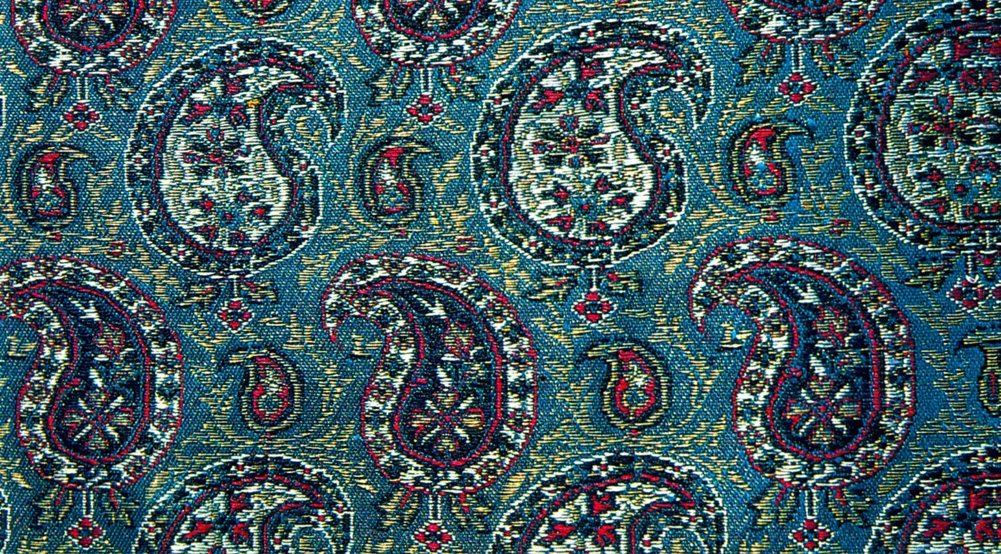 Close-up of detailed blue paisley fabric pattern with red, white, and yellow intricate floral and teardrop shapes.