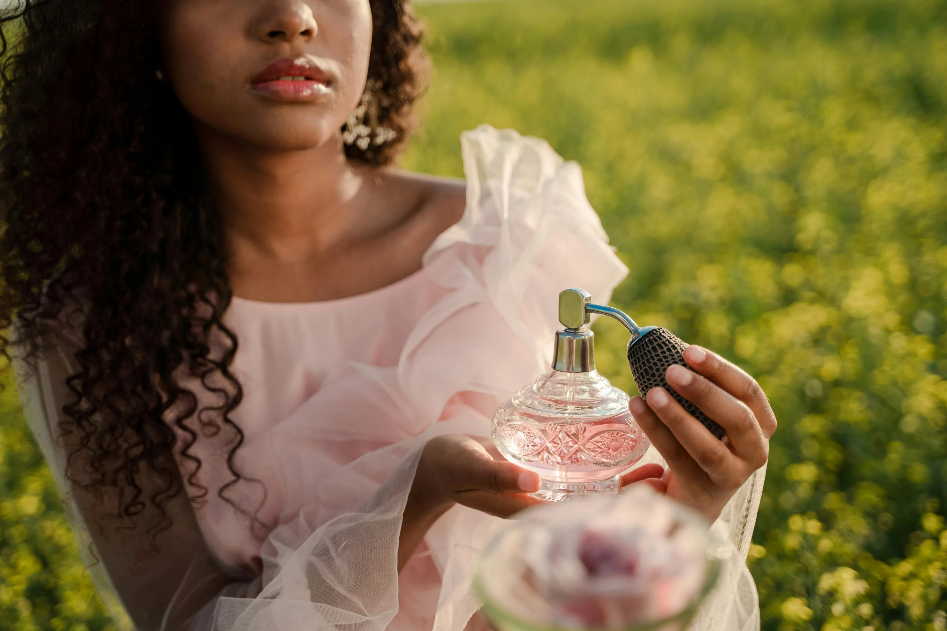 Woman in a pink dress holding a vintage perfume bottle, evoking memories with mom's perfume in a sunlit garden.