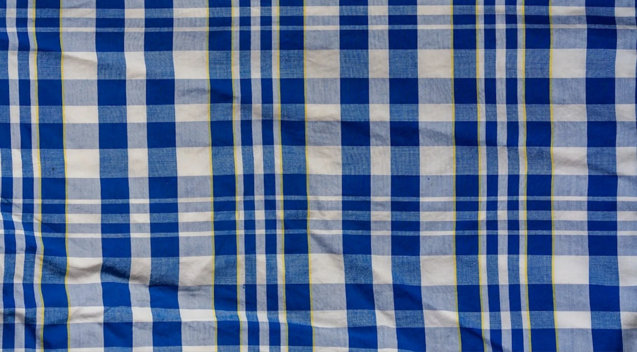 Blue and white plaid fabric with yellow and green thin stripes forming a classic checkered pattern on cloth.