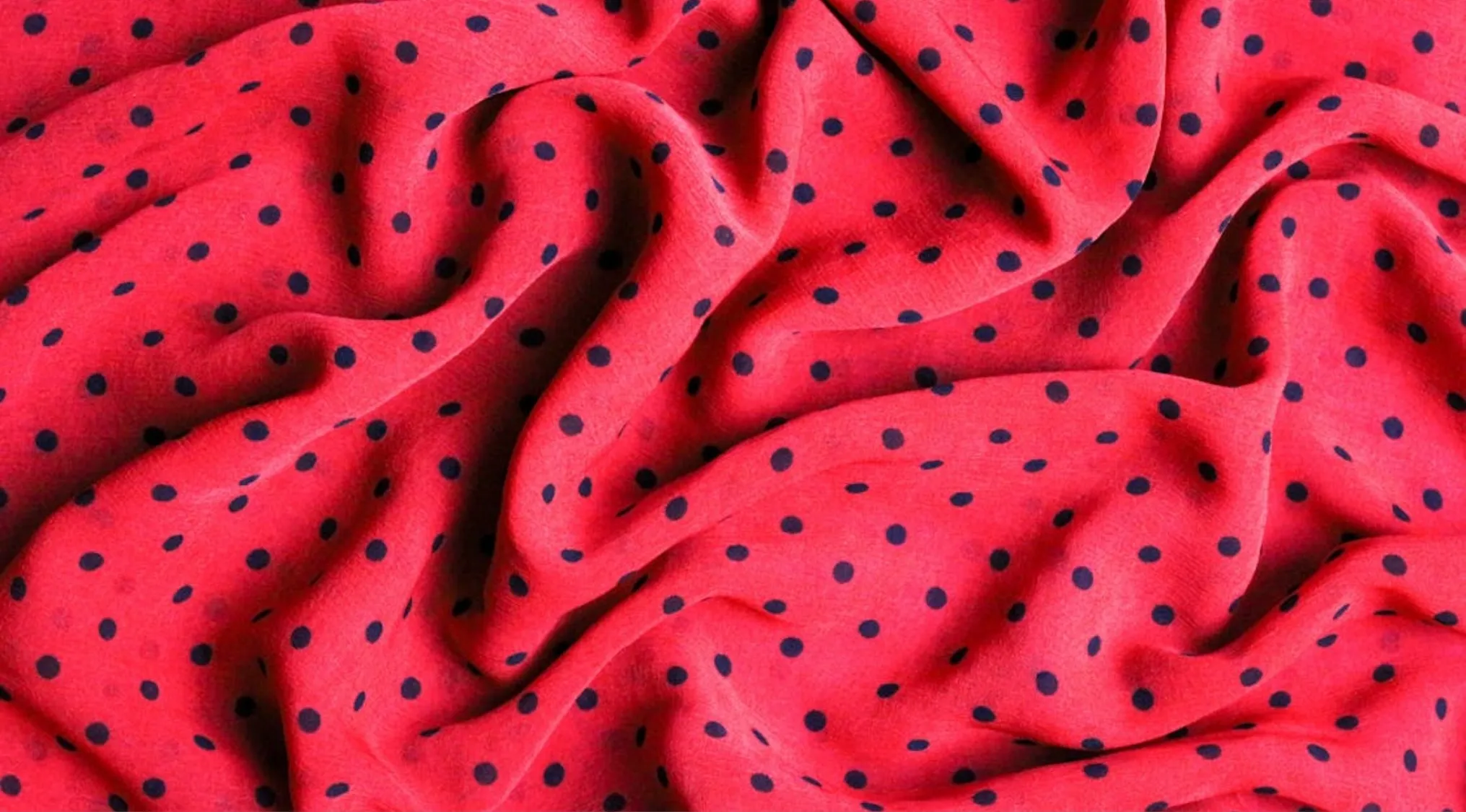 Red fabric with black polka dots arranged in a classic pattern, draped with visible folds and texture.