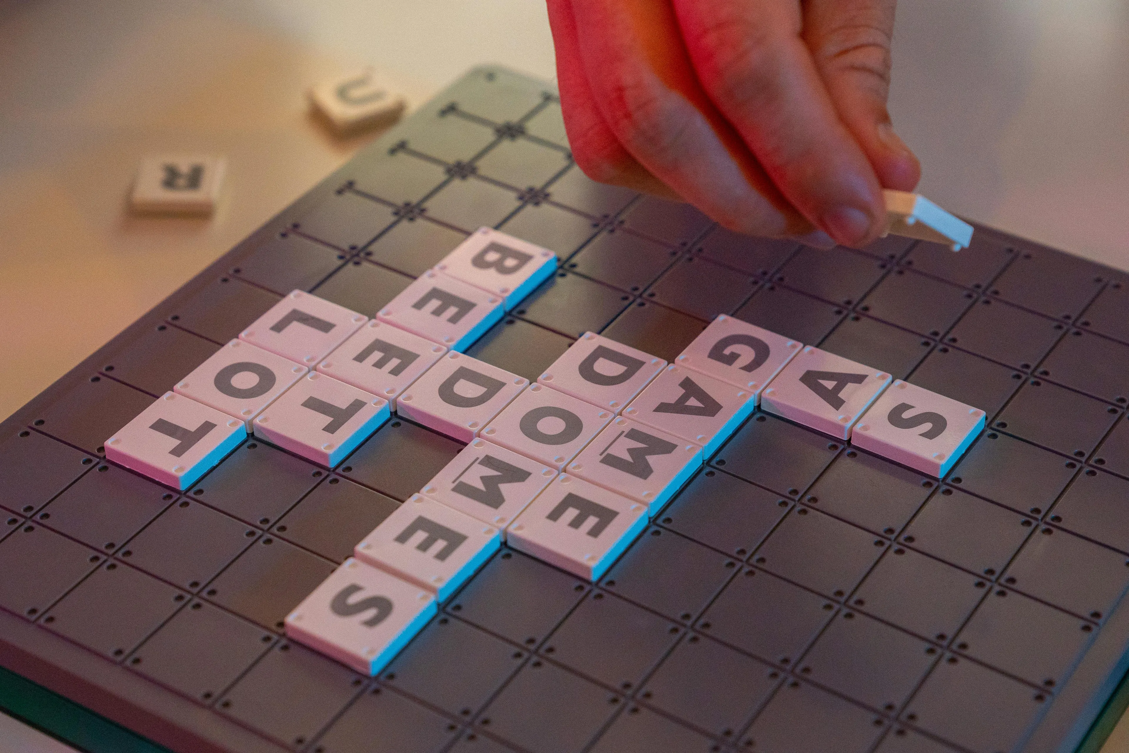 Hand placing letter tiles on a Scrabble board with words forming a crossword pattern in a game setting.